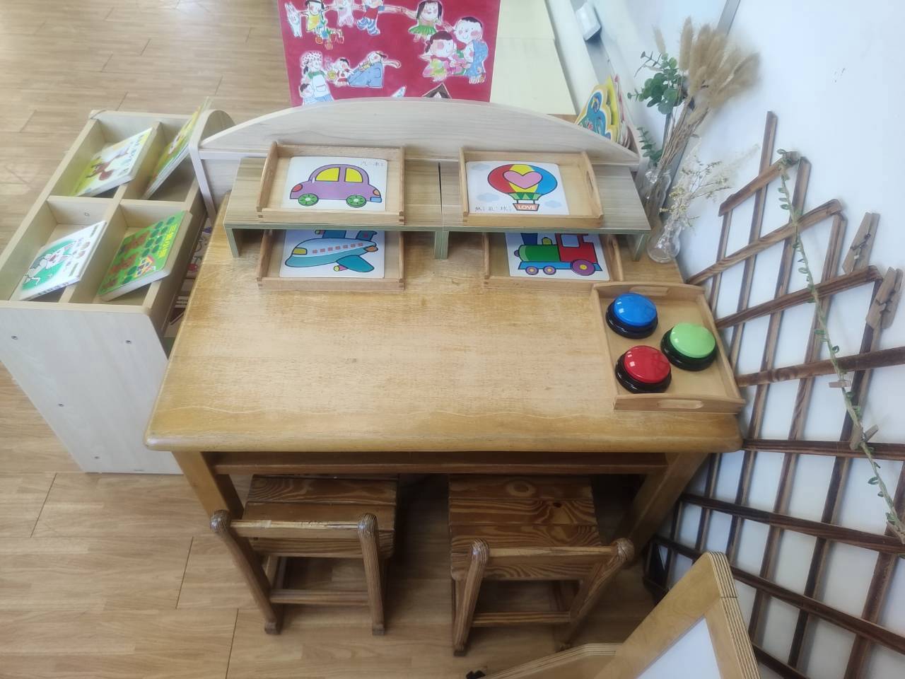 桌上放有交通工具（汽車、飛機、熱氣球、火車）的木質拼圖板，以及一組紅綠藍黑四色的音效按鈕（Buzzers），屬於益智區內的操作與邏輯配對桌遊。